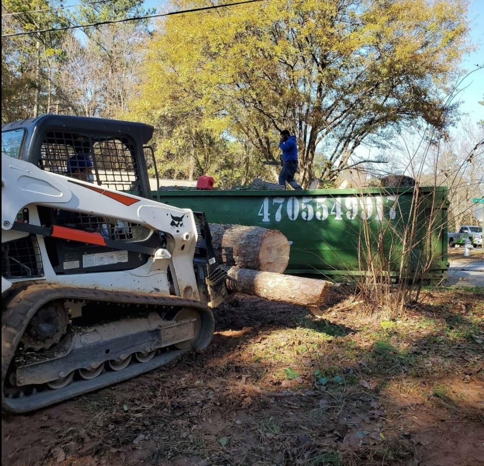 A bobcat machine pushing logs into an IEG Disposal roll-off dumpster for debris removal in Canton, GA.