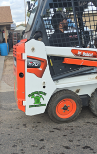 A Bobcat S70 skid-steer loader with ALL around junk, LCC branding, used for demolition and hauling in Mesa, AZ.