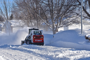 A Bobcat compact track loader with a snow blower clearing a residential street, a service from Handyman Rental in Portland, ME.