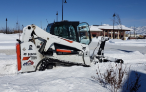 A Bobcat compact track loader with a snow blower attachment clearing deep snow, rented from Handyman Rental in Portland, ME.