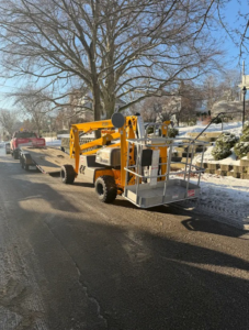 A yellow boom lift being towed on a trailer, ready for a job from Handyman Rental in Portland, ME.