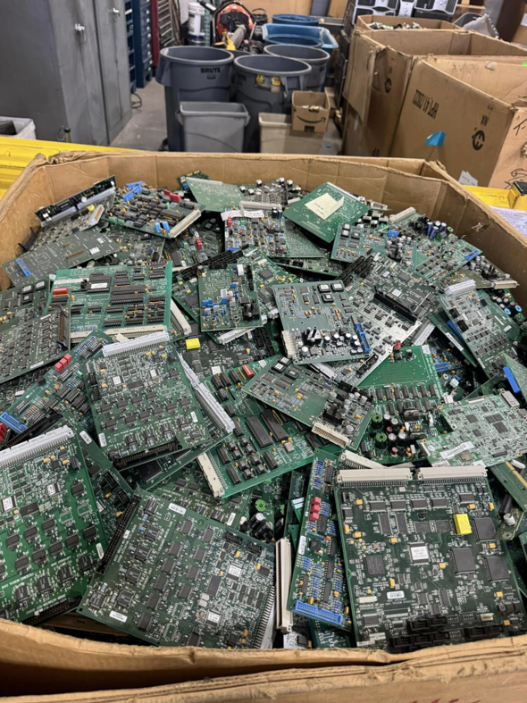 A large cardboard box filled with green circuit boards and other electronic waste at E-Z Money Recycling LLC in Phoenix, AZ.
