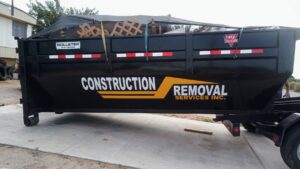 A branded dump trailer from Construction Removal Services Inc. in El Paso, TX, filled with various junk and covered with a tarp.