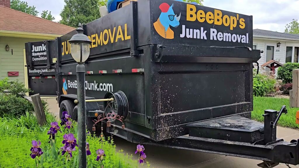 A BeeBop's Junk Removal branded trailer with junk inside, parked in a residential driveway in Sioux Falls, SD.