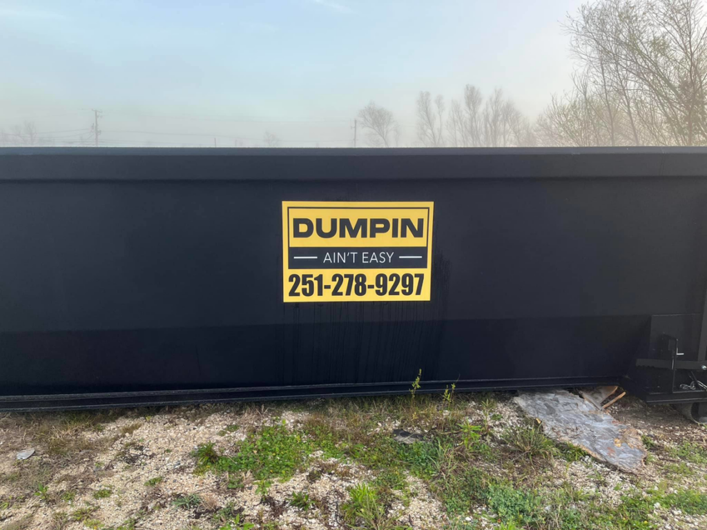 A black roll-off dumpster with the Dumpin Ain't Easy logo and phone number in Westwego, LA.