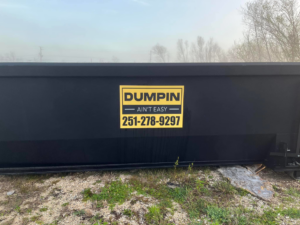 A black roll-off dumpster with the Dumpin Ain't Easy logo and phone number in Westwego, LA.