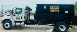 A white roll-off truck with a black dumpster, branded with Dumpin Ain't Easy logo, parked in Westwego, LA.