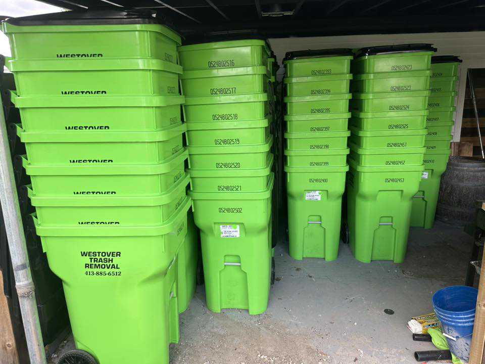 Stacks of bright green branded trash bins ready for service from Westover Trash Removal in Springfield, MA.