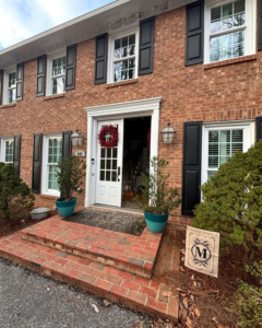 The exterior of a classic brick house with black shutters and a welcoming front door by Welcome Home Building Services in Winston-Salem, NC.
