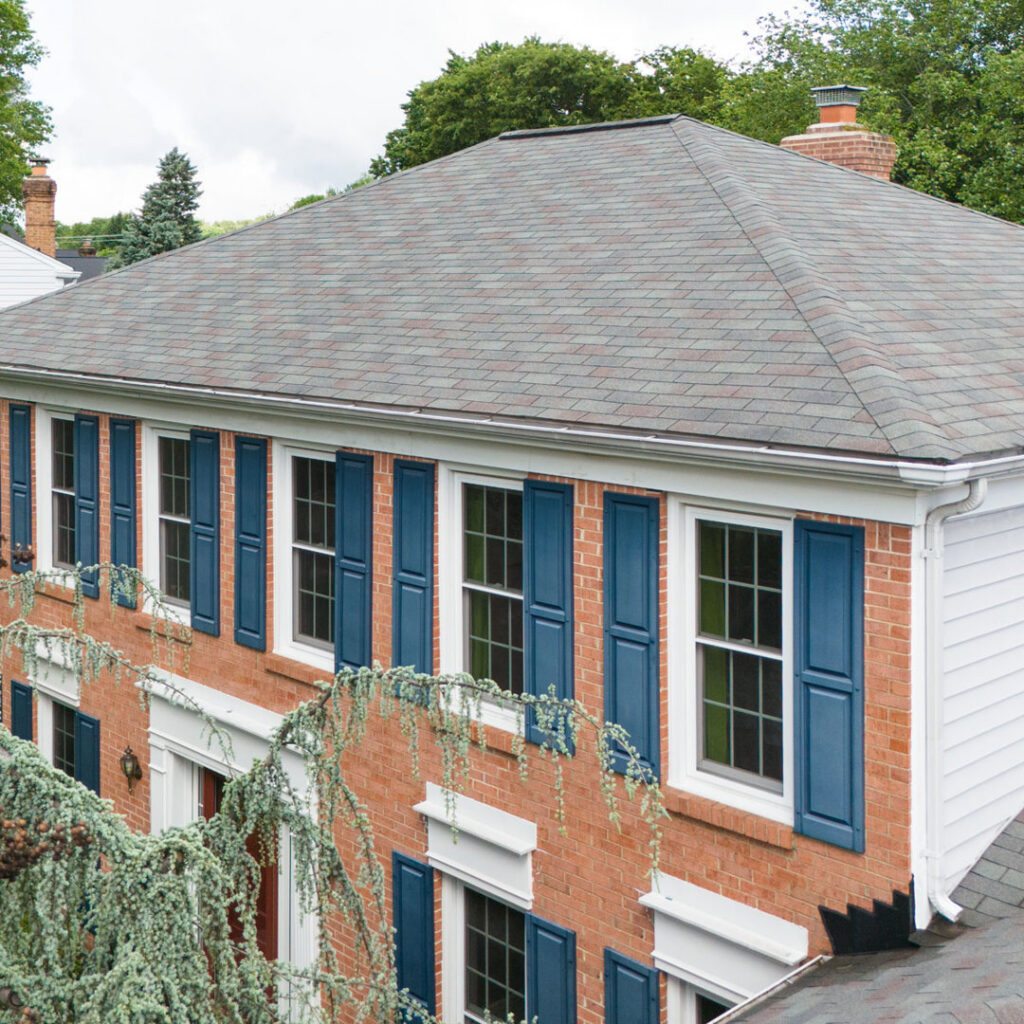 A brick house featuring a new roof and blue shutters, showcasing exterior home improvement by Four Seasons Home Improvement Company, Inc. in Rockville, MD.