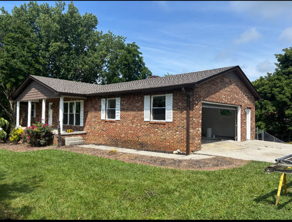 Brick house with a new roof and gutters, with equipment visible, showing work by Knoxville Guttering and Home Improvements in Knoxville, TN.