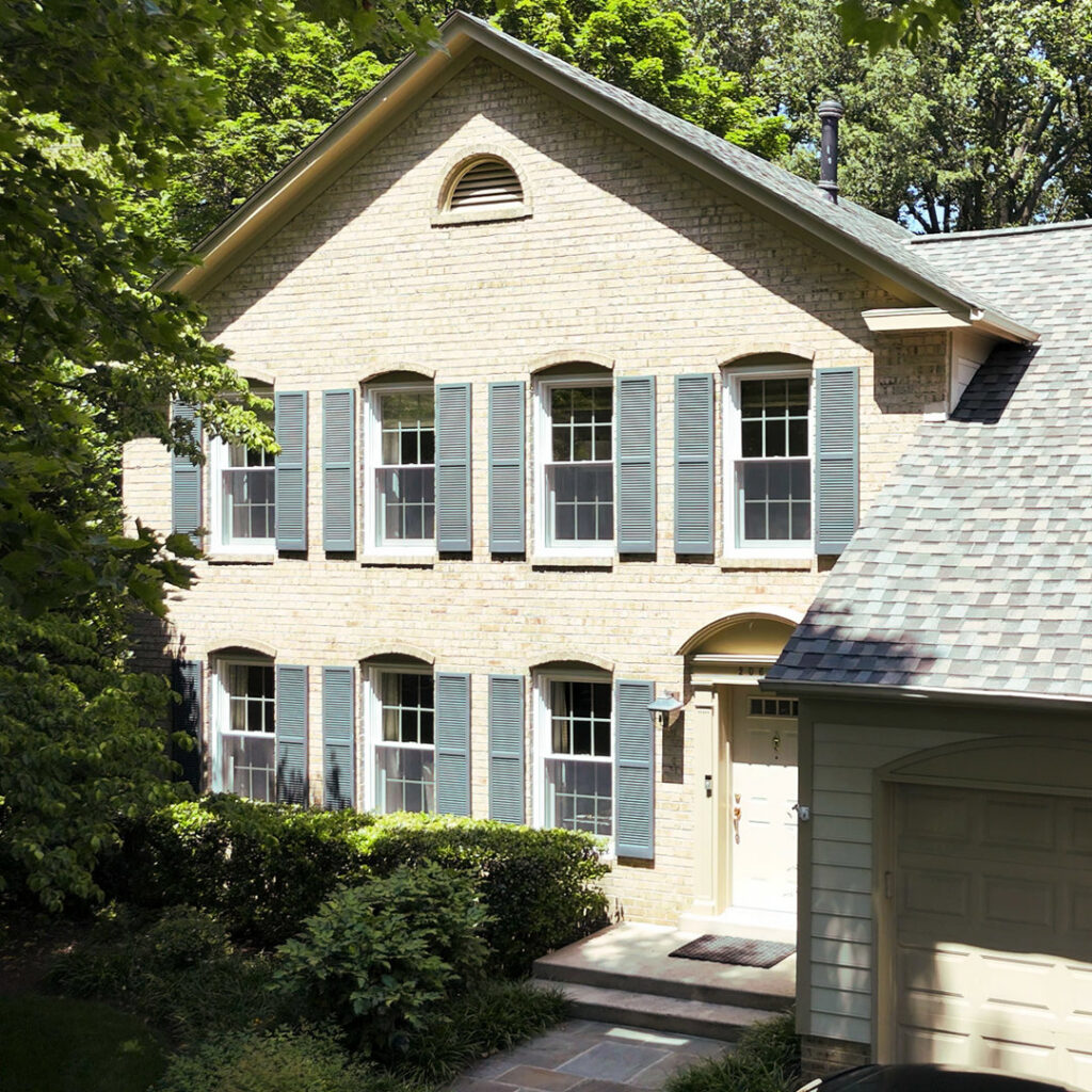 A brick house with newly installed windows and shutters, showcasing exterior home improvement by Four Seasons Home Improvement Company, Inc. in Rockville, MD.
