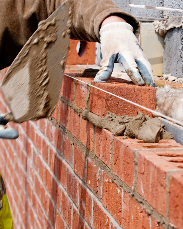 A construction worker laying bricks with mortar, showcasing work by Pigliavento Associates, LLC in Schenectady, NY.