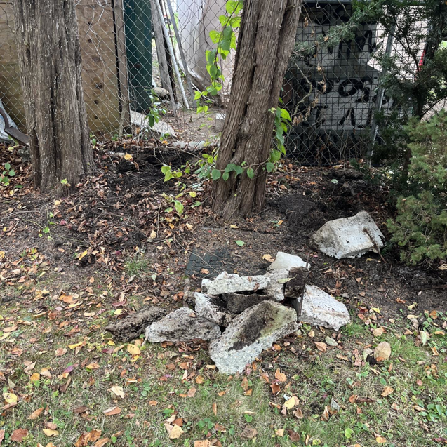 Broken concrete pieces scattered on the ground near trees and a fence, ready for removal by DLS Junk Removal in Waterbury, CT.