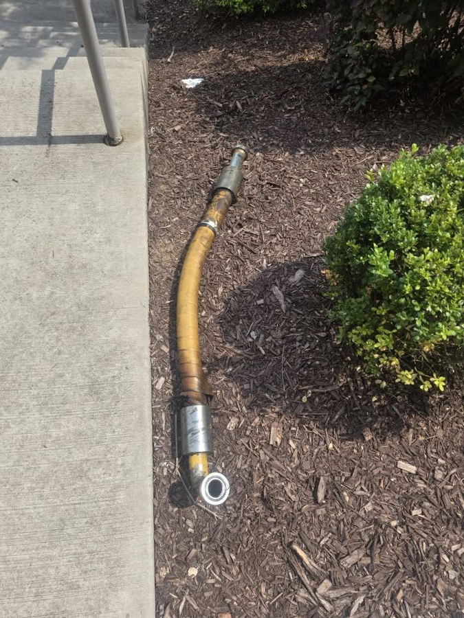A broken hydraulic hose lying on the ground, indicating a repair job by Wise Equipment Services in Rock Hill, SC.