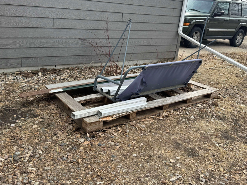 A broken patio swing, wooden pallets, and metal gutters piled outside a house, ready for junk removal by Quality Rent & Removal in Minot, ND.