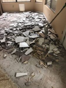 A large pile of broken tiles and flooring debris in a room, ready for removal by Junk Junkees in Peoria, AZ.