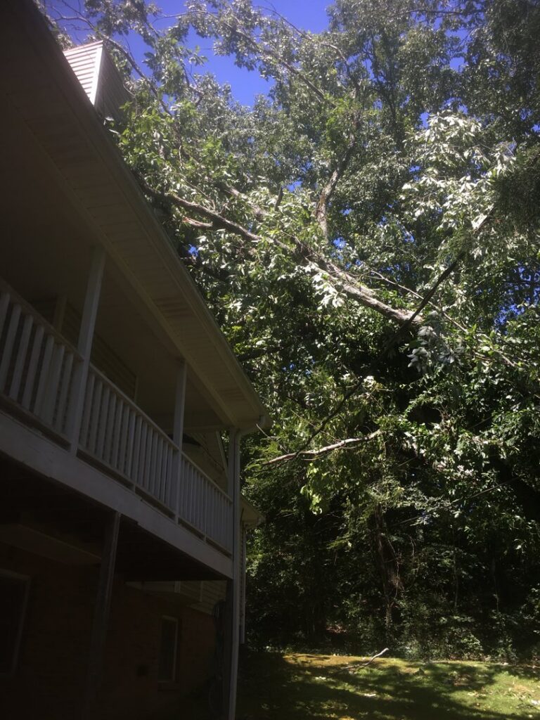 Large broken tree branch hanging over a house, indicating emergency tree service work by Jon's Tree Service in Pelham, AL.