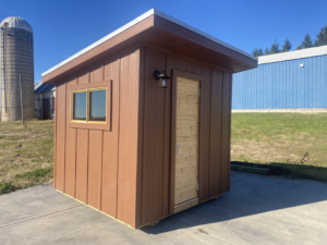 Completed brown tiny home or sauna exterior with a wooden door, window, and outdoor light by No Boundaries Tiny Homes in Eau Claire, WI
