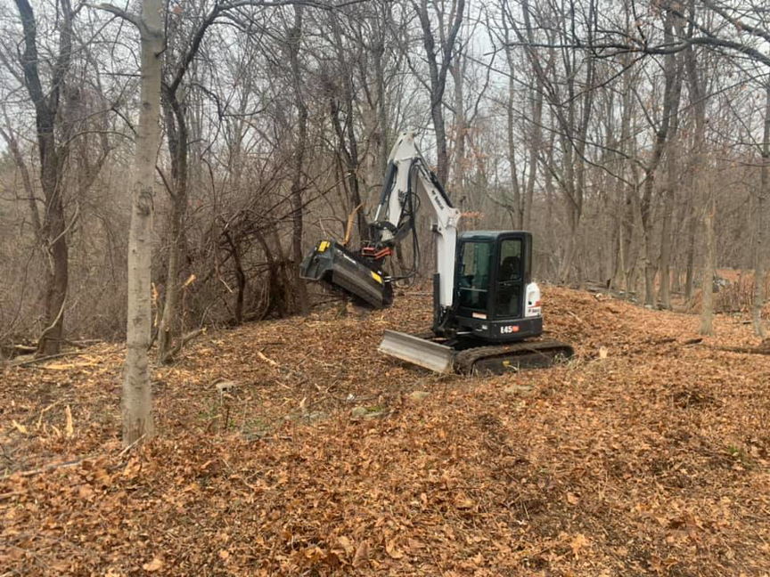 An excavator with a mulching attachment clearing brush and small trees for land preparation by L & P Excavation and Tree Removal in Salem, NH.