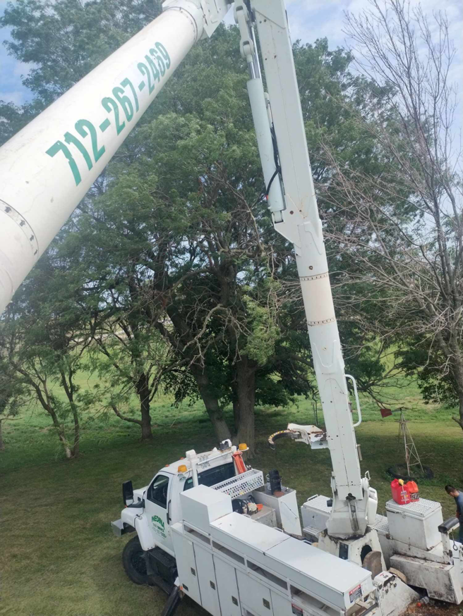 A white bucket truck extended high towards trees, ready for trimming by Javier Medina Tree Service LLC in DrDenison, IA.
