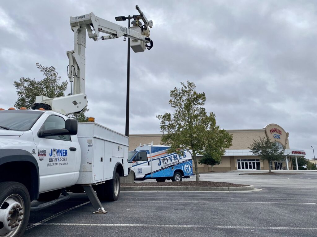 A Joyner Electric And Security bucket truck repairing a street light in a parking lot in Savannah, GA.