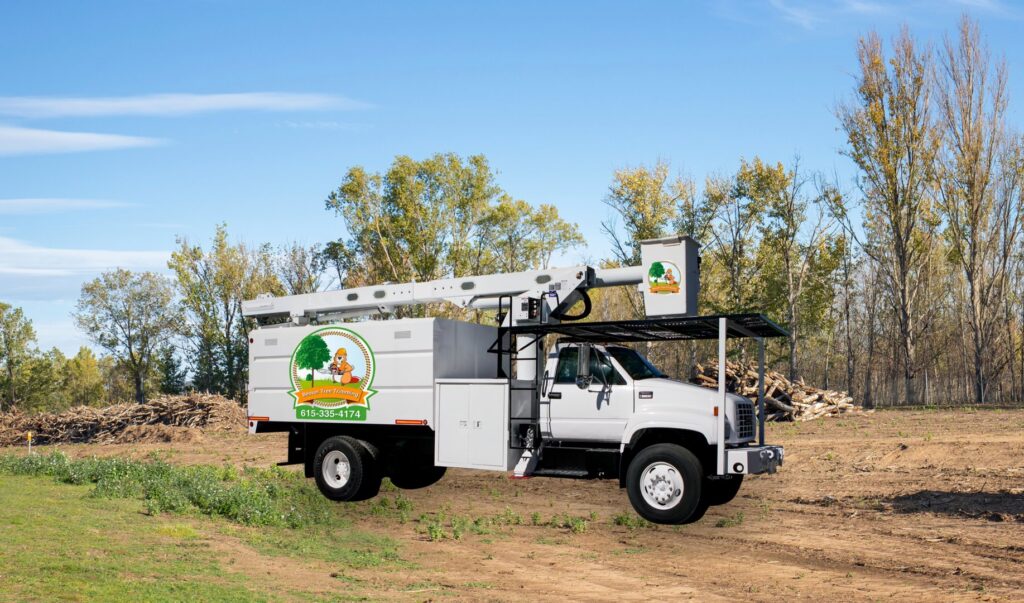 A white bucket truck and piles of wood debris after a tree service job by Beaver Stump and Tree Service in Antioch, TN