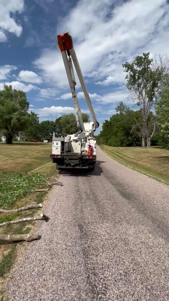 A bucket truck parked on a road with cut tree branches, indicating tree trimming cleanup by Happy Lemon Tree Service in Belton, MO.