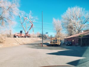A bucket truck performing tree trimming services by a roadside for R and J Tree Service in Farmington, NM.