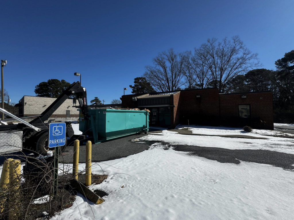 A Budget Boxx dumpster filled with debris outside a commercial building, indicating junk removal in Suffolk, VA.