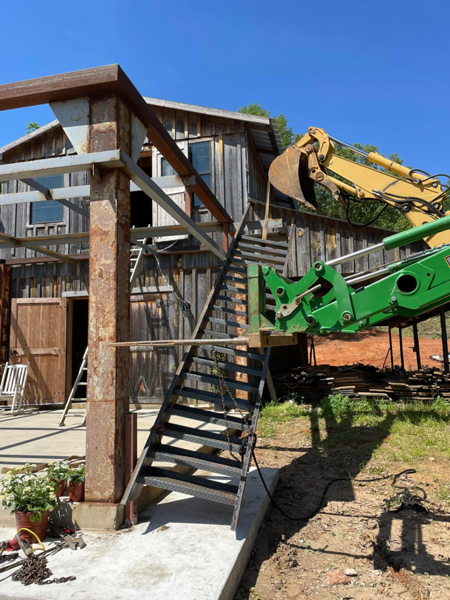 A building under construction with metal stairs and an excavator in the background, managed by SJ Construction Services LLC in Austin, TX.