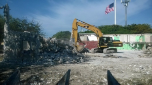 A large yellow excavator demolishing a building, showing a general contractor job by Allied Demolition Inc. in Miami, FL.