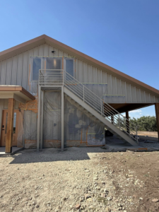 The exterior of a building with metal siding and a newly installed metal staircase, indicating ongoing construction by Javier's Painting in San Angelo, TX.