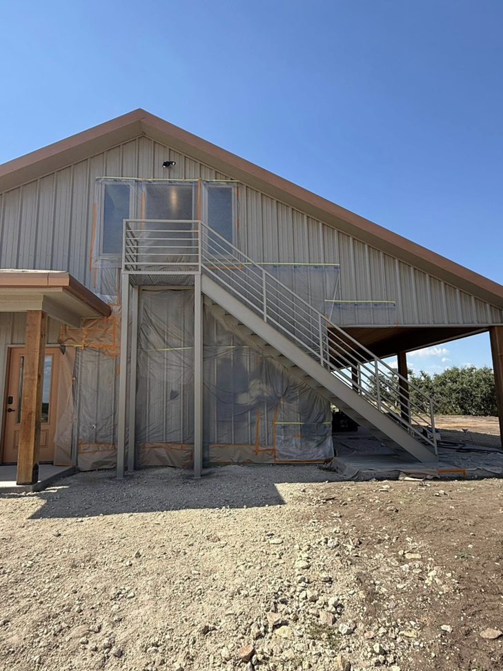 The exterior of a building with metal siding and a newly installed metal staircase, indicating ongoing construction by Javier's Painting in San Angelo, TX.