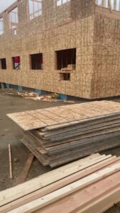 Building exterior with plywood sheathing and stacks of lumber on a construction site by LCM FRAMING LLC in Danbury, CT