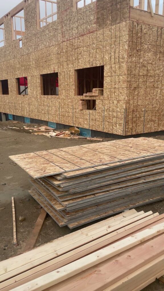 Building exterior with plywood sheathing and stacks of lumber on a construction site by LCM FRAMING LLC in Danbury, CT