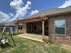 A newly built wooden pergola and deck attached to a brick house by Old Things Created New Handyman Service in Springdale, AR.