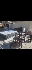 A large mattress, chairs, a table, and a couch placed outside a garage for removal by The Junkporter Junk Removal in Las Vegas, NV.