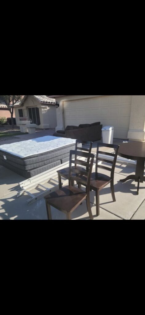A large mattress, chairs, a table, and a couch placed outside a garage for removal by The Junkporter Junk Removal in Las Vegas, NV.