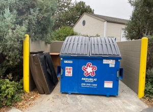 A large piece of bulky furniture leaning against a wall next to a dumpster, ready for removal by United Trash Valet in Seattle, WA.