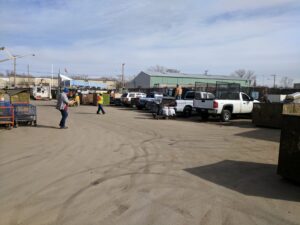 A busy outdoor recycling yard with multiple trucks, dumpsters, and workers at Get Green Recycling Co. in Aurora, IL.