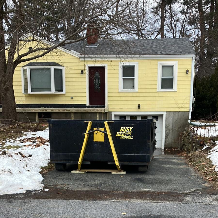 A BusyBee Disposal dumpster placed in front of a yellow residential house in Everett, MA, for waste disposal.