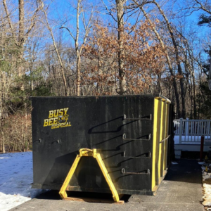 A BusyBee Disposal dumpster placed in a residential yard with trees and snow in Everett, MA, for junk removal.