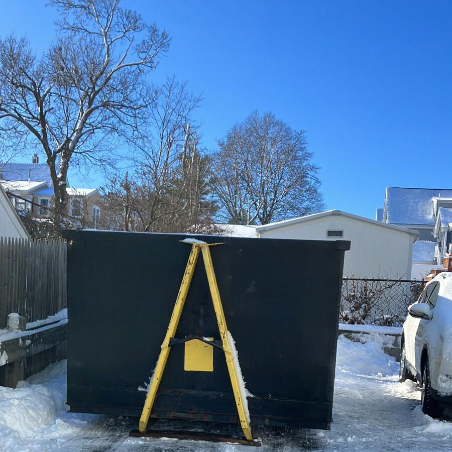 A BusyBee Disposal dumpster positioned in a snowy residential area in Everett, MA, for waste collection.
