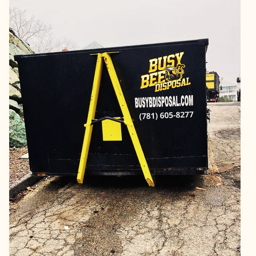 A large black and yellow BusyBee Disposal dumpster placed on a paved surface in Everett, MA, ready for junk removal.