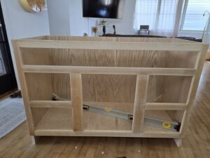 An unfinished wooden cabinet frame with a level inside, showing assembly in progress by Just-In-Time Handyman Services in Honolulu, HI.