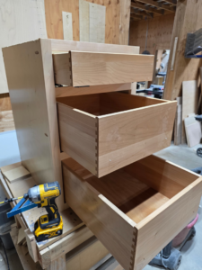 Cabinet installation in progress, showing wooden drawers with dovetail joints and a power drill, by Prestige Statewide, LLC in Eugene, OR.