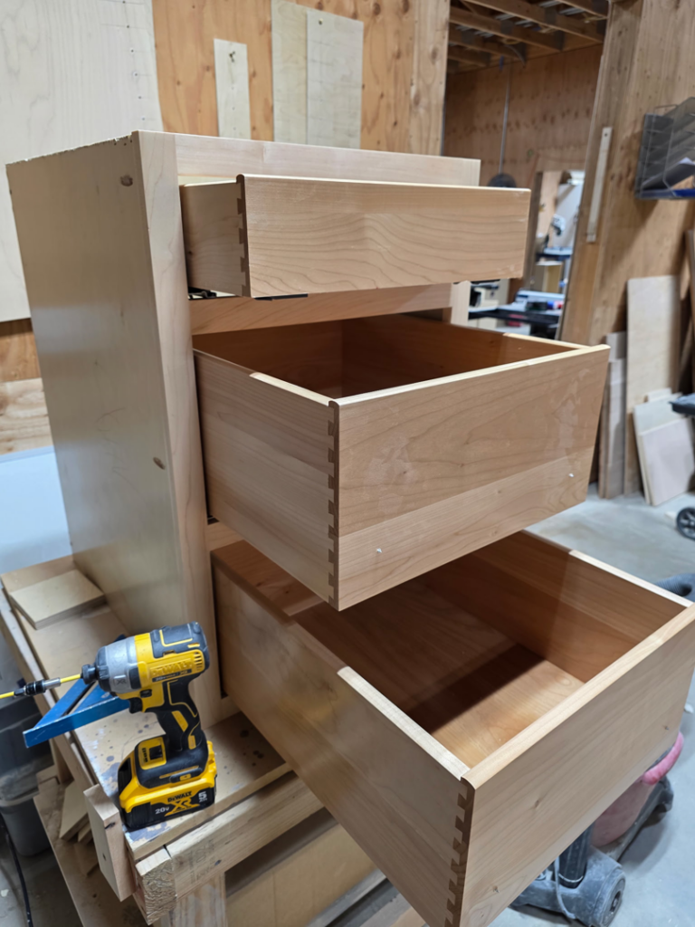 Cabinet installation in progress, showing wooden drawers with dovetail joints and a power drill, by Prestige Statewide, LLC in Eugene, OR.