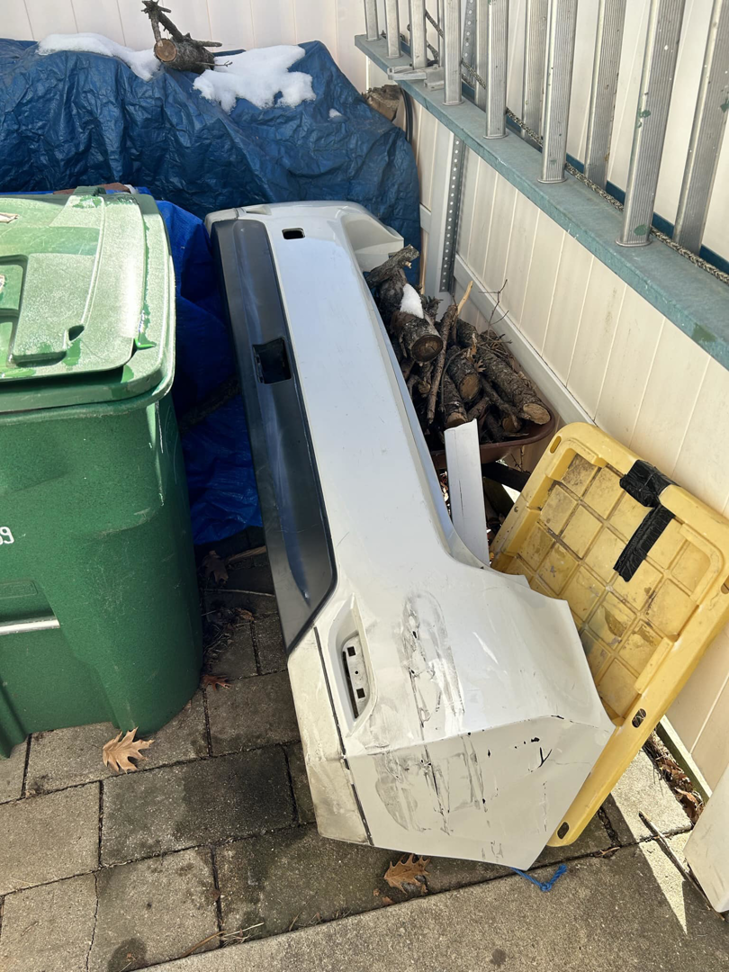 A pile of miscellaneous junk including a car bumper and logs next to a green bin, ready for removal by Custom Roll-Off Solutions in Des Moines, IA.