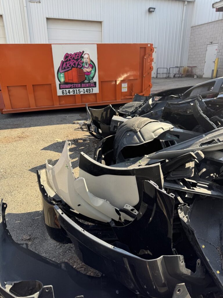 A Crazy Larry's Dumpster Rental dumpster next to a large pile of car parts for junk removal in Columbus, OH.